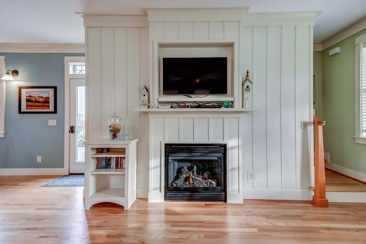 A warm, intimate sitting area centered around a gas fireplace, complemented by bookshelves and a television. The inviting setting encourages shared laughter, quiet moments with a book, or watching a favorite film together after a day at the beach.