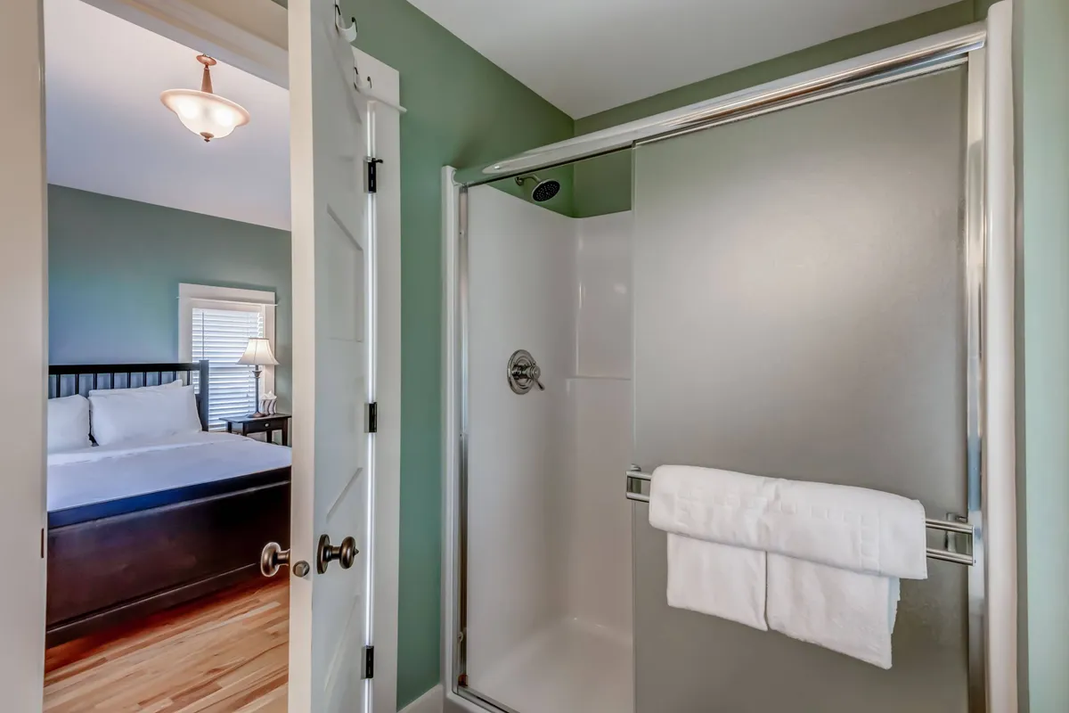 A calming view of an ensuite bathroom with a glass-enclosed shower, plush towels, and a glimpse of the adjoining bedroom in the background, seamlessly connecting rest and refreshment spaces.