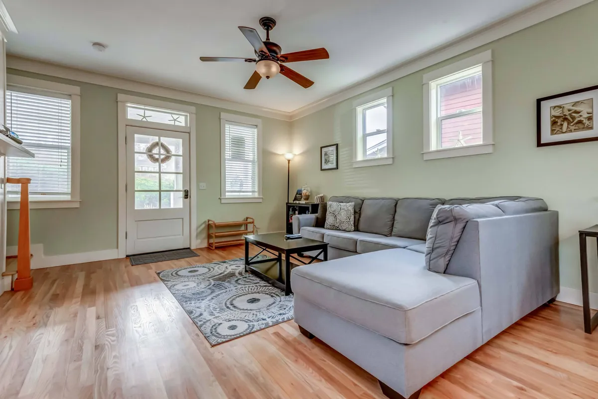 This inviting living room scene features a plush sofa arranged around a coffee table, with the front door and decorative wall art visible in the background. Soft lighting from a table lamp creates a cozy ambiance, while natural light filters in, highlighting the welcoming atmosphere.
